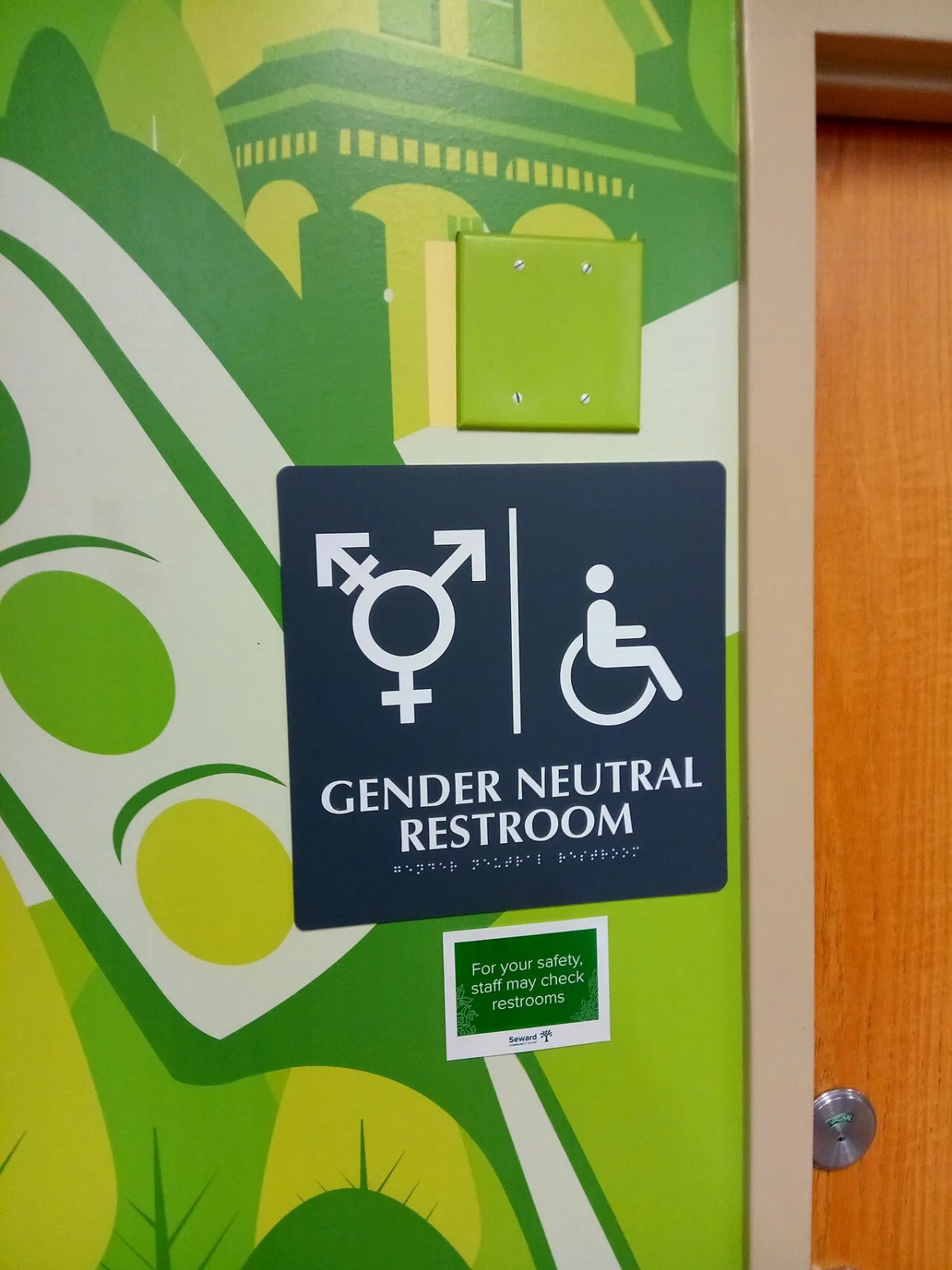 Donker bordje met pictogrammen, de tekst Gender Neutral Restroom en braille, naast een deur